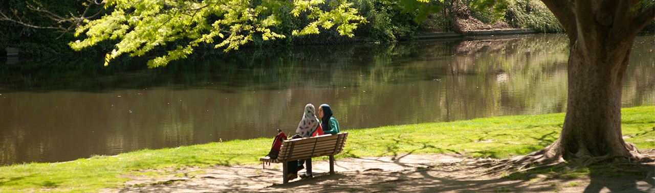 students sitting on bench in front of spafford lake in spring