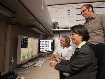 three people sitting around computer monitor