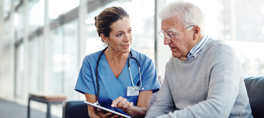 Female nurse sits next to older man with delirium and points at tablet