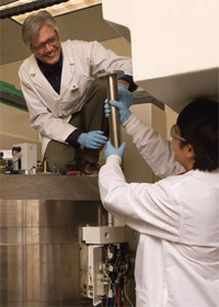 PHOTO — Dave Kukis (left) and Lina Planutyte manage the daily responsibilities of running a cyclotron and producing the short-lived radioisotopes necessary for Sutcliffe's research program.